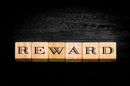Word Reward. Wooden small cubes with letters isolated on black background.Concept image.