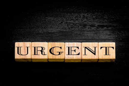 Word urgent. Wooden small cubes with letters isolated on black background.Concept image.