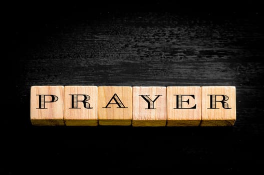 Word Prayer. Wooden small cubes with letters isolated on black background.Concept image.