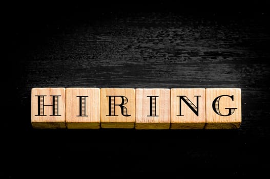 Word Hiring. Wooden small cubes with letters isolated on black background.Concept image.