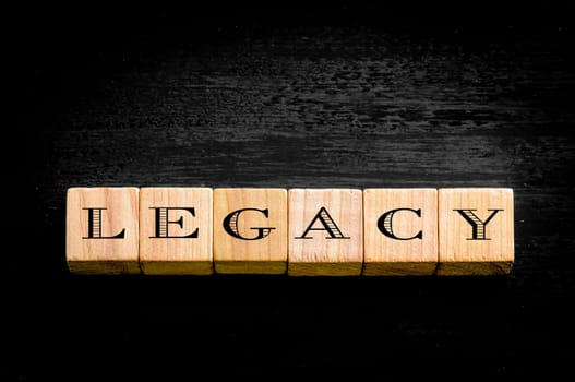 Word Legacy. Wooden small cubes with letters isolated on black background.Concept image.