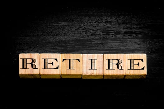 Word Retire. Wooden small cubes with letters isolated on black background.Concept image.