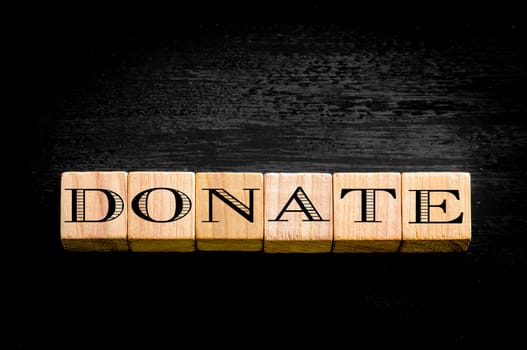 Word Donate. Wooden small cubes with letters isolated on black background.Concept image.