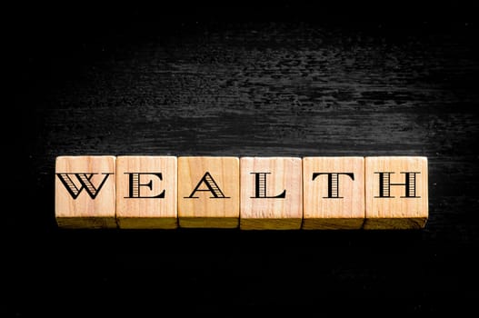 Word Wealth. Wooden small cubes with letters isolated on black background.Concept image.
