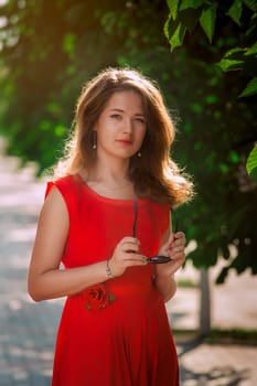 Portrait of a beautiful sexy fashion girl in a red dress on the nature of the park, with dark hair and a leather belt