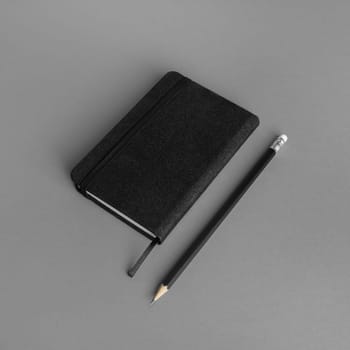 Blank black notepad and pencil on gray paper background.