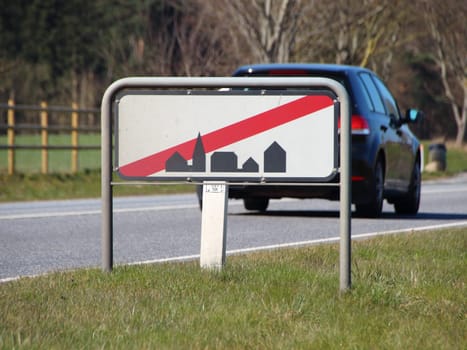 A traffic sign signifying leaving town. A car is directly behind the sign.