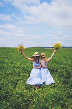 Two beautiful girlfriends in hats hugging in a green field, a postcard under the old-fashioned.