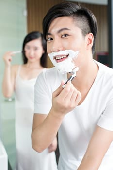 Young Chinese couple doing makeup and shaving beard in washroom