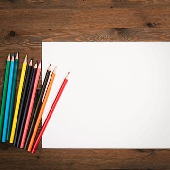 The sheet is pure white and colored pencils for drawing on a wooden background with a place to copy. Mock-up, mockup, layout.