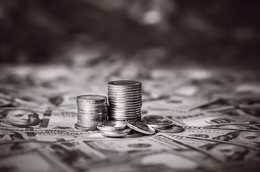 Stacks of coins against the background of hundred-dollar bills are scattered throughout the space. The coins are collected in two columns, some scattered. Black and white.