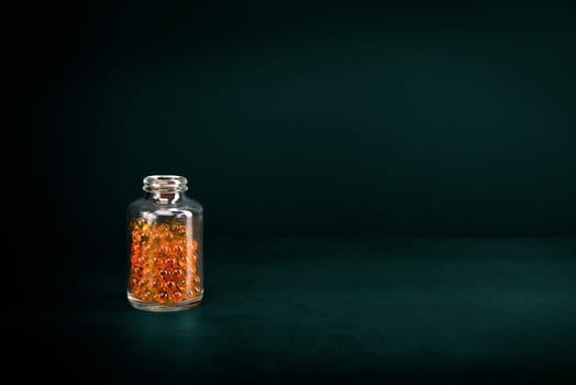 A glass jar with pills of bright orange yellow color on a green background. Place for the label, logo, layout.