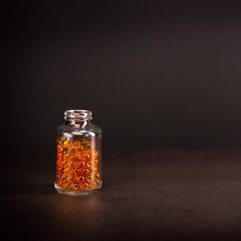 A glass jar with pills of bright orange yellow color on a brown background. Place for the label, logo, layout.