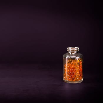 A glass jar with pills of bright orange yellow color on a lilac background. Place for the label, logo, layout.