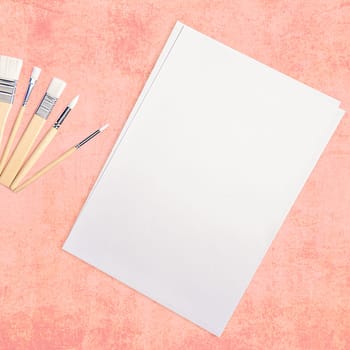 A clean white sheet and brushes on a textured pink background with space to copy. Layout, mockup, layout.