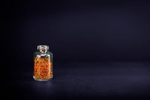 A glass jar with pills of bright orange yellow color on a purple background. Place for the label, logo, layout.