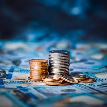 Stacks of coins against the background of hundred-dollar bills are scattered throughout the space. The coins are collected in two columns, they are shiny, golden in color.