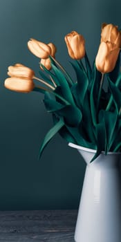 Tulips in a jug. Classic still life with a bouquet of delicate tulip flowers in a vintage white jug on a green background and an old wooden table. Art photography.