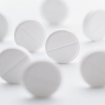 A pile of white pills scattered on a bright white background. Selective focus. Mockup layout, template.