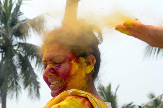 Portrait Of One Young Indian Happy woman with pink, yellow and red Holi colored powder paint on face During Holi Color festival. Front View. Looking at camera.