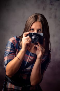Girl photographer peeking out from behind the camera, half-length studio portrait on a gray background