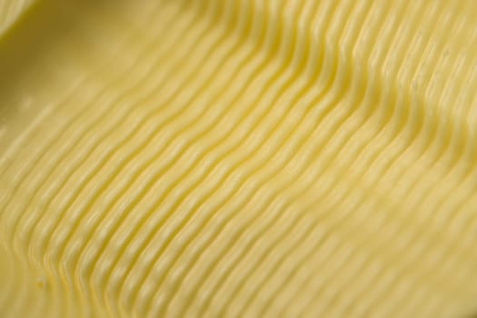 Wavy ripple pattern in butter created by a serrated butter knife. Full frame abstract food texture background, taken as a super macro close up.