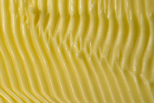 Food themed background of margarine. Shaped into detailed yellow grooves by a serrated kitchen knife used to spread it on bread. Full frame texture.
