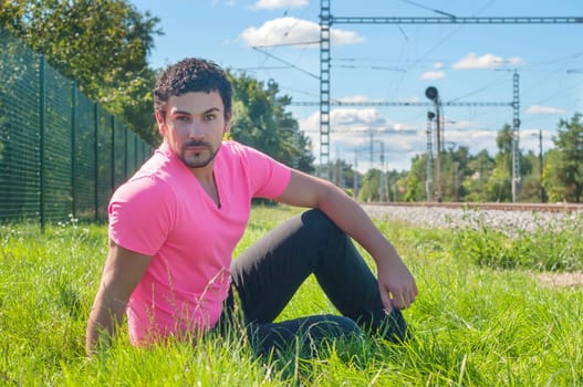 Young guy an in orange sitting on the grass near railway