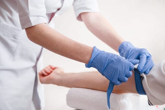 Nurse fastens the medical tourniquet on arm before taking blood test.