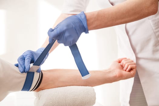 Nurse fastens the medical tourniquet on arm before taking blood test.