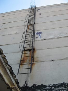 An old rusty staircase to the roof of the building. Abandoned industrial object.