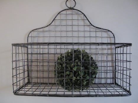 Stylish wire basket on wall with round boxwood ball