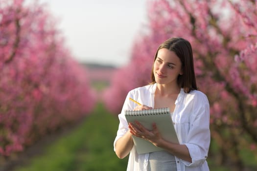 Happy woman drawing on notebook in a pink flowered field in spring