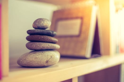 Feng Shui: Stone cairn at home in a book shelf, blurry books in foreground and background. Balance and relaxation.