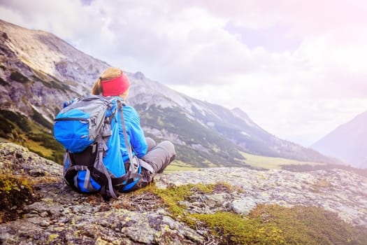 Woman in sportswear and with backpack is sitting on the stony ground and enjoys the view, in the mountains