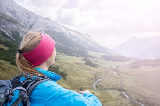 Woman in sportswear and with backpack enjoys the view in the mountains