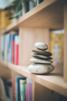 Feng Shui: Stone cairn at home in a book shelf, blurry books in foreground and background. Balance and relaxation.