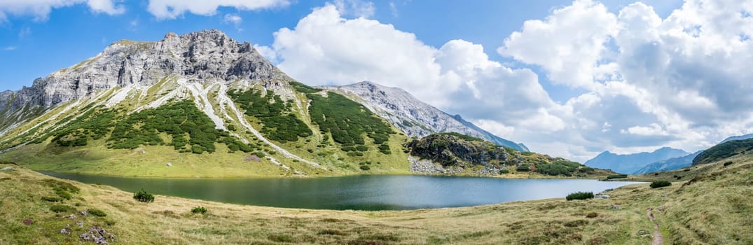 Mountain landscape: Rocky mountain range, clear water lake and blue cloudy sky  Panorama
