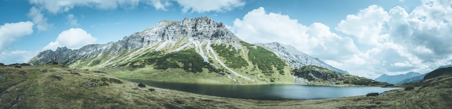 Mountain landscape: Rocky mountain range, clear water lake and blue cloudy sky  Panorama