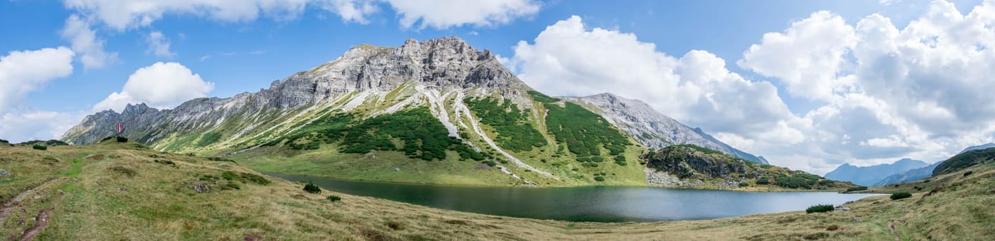 Mountain landscape: Rocky mountain range, clear water lake and blue cloudy sky  Panorama