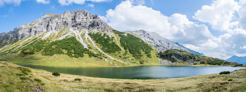 Mountain landscape: Rocky mountain range, clear water lake and blue cloudy sky  Panorama