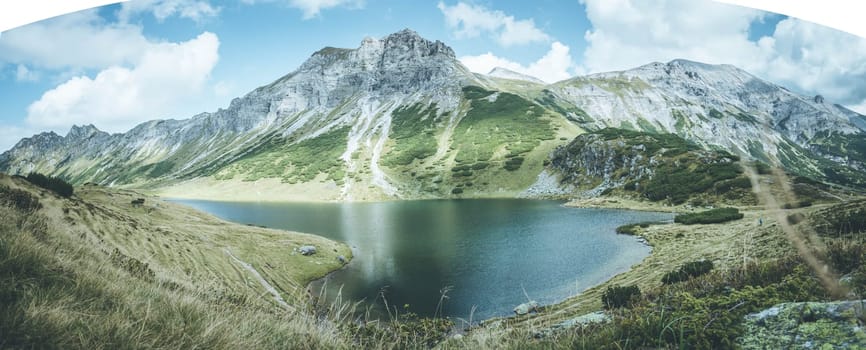 Mountain landscape: Rocky mountain range, clear water lake and blue cloudy sky  Panorama
