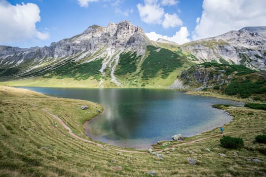Mountain landscape: Rocky mountain range, clear water lake and blue cloudy sky