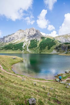 Mountain landscape: Rocky mountain range, clear water lake and blue cloudy sky