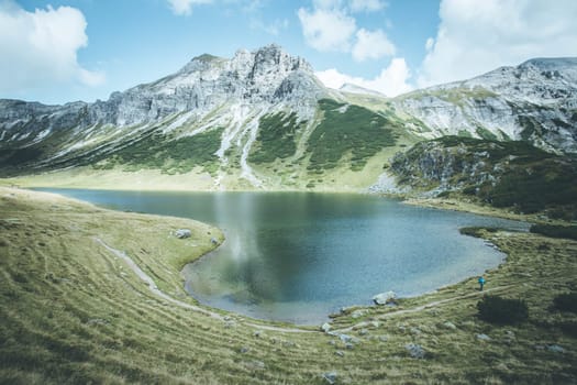 Mountain landscape: Rocky mountain range, clear water lake and blue cloudy sky