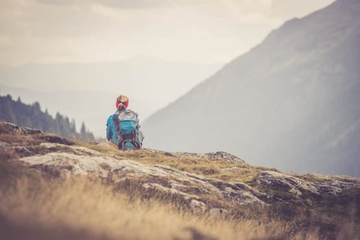 Woman in sportswear and with backpack is sitting on the stony ground and enjoys the view, in the mountains