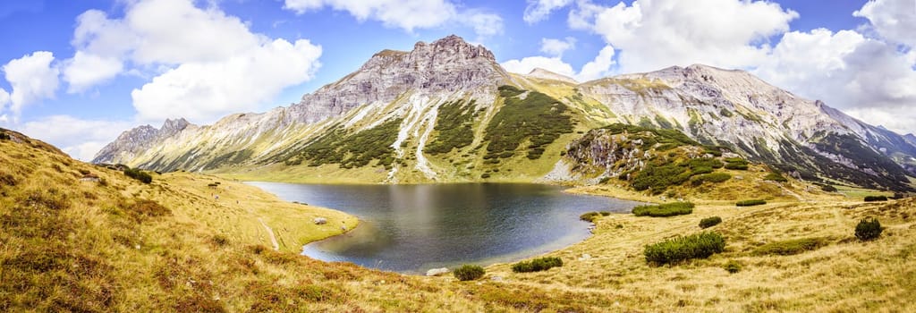 Mountain landscape: Rocky mountain range, clear water lake and blue cloudy sky  Panorama