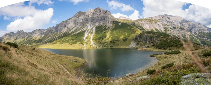 Mountain landscape: Rocky mountain range, clear water lake and blue cloudy sky