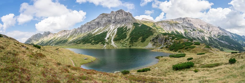 Mountain landscape: Rocky mountain range, clear water lake and blue cloudy sky  Panorama