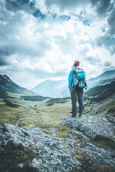 Woman in sportswear and with backpack enjoys the view in the mountains